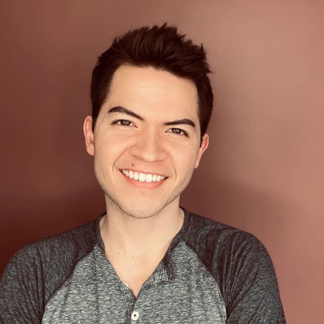 image of derek in front of red background wearing gray shirt smiling at camera